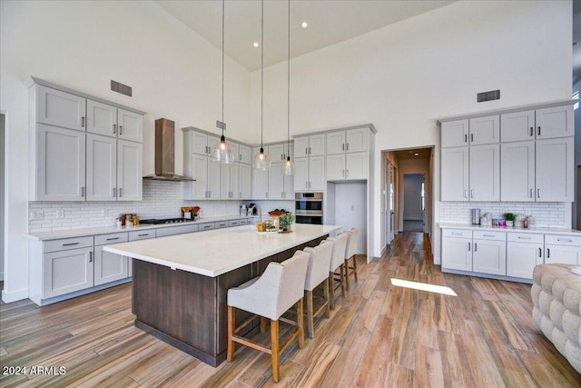 kitchen featuring a breakfast bar area, a kitchen island with sink, pendant lighting, hardwood / wood-style floors, and wall chimney range hood