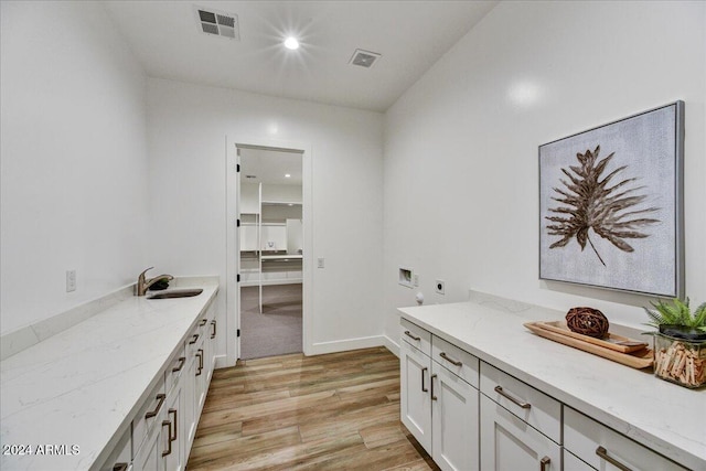 interior space with sink, light stone countertops, light hardwood / wood-style floors, and white cabinets