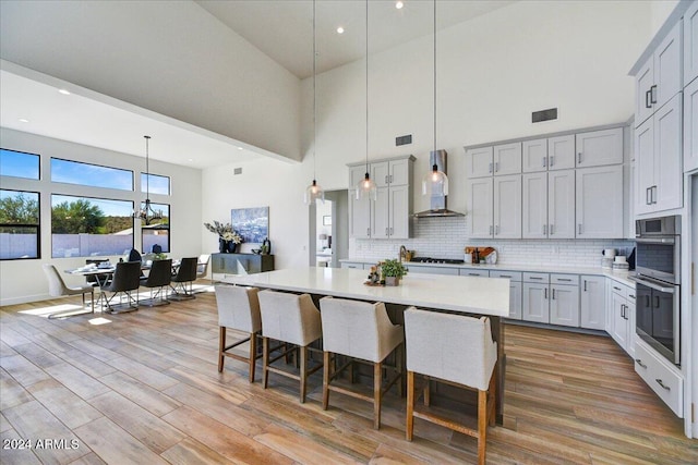 kitchen with hanging light fixtures, a large island, wall chimney range hood, and decorative backsplash