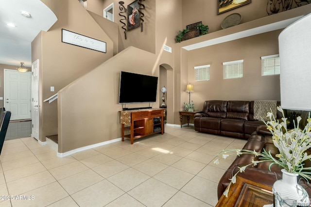 living area featuring baseboards, stairway, light tile patterned floors, and arched walkways