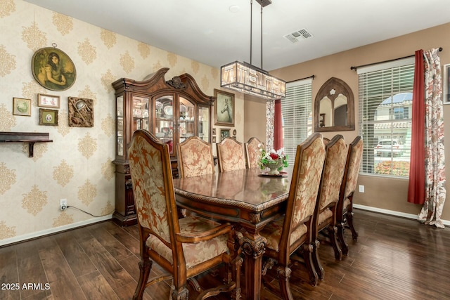 dining space with dark wood-type flooring, visible vents, wallpapered walls, and baseboards