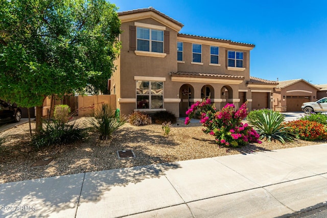 mediterranean / spanish home featuring a garage, stucco siding, a tiled roof, and fence