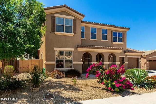 mediterranean / spanish home with a tile roof, a garage, stucco siding, and fence