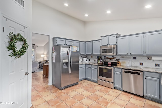 kitchen featuring high vaulted ceiling, light stone counters, appliances with stainless steel finishes, and light tile patterned floors