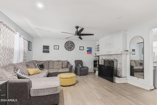 living room with light hardwood / wood-style flooring, a tiled fireplace, and ceiling fan