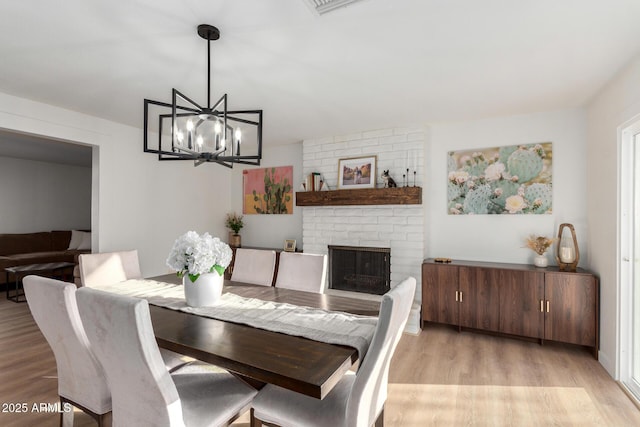 dining room featuring a chandelier, a brick fireplace, and light wood-style floors