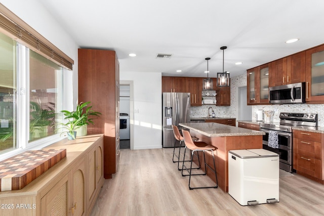 kitchen with light wood-type flooring, visible vents, a sink, a center island, and appliances with stainless steel finishes