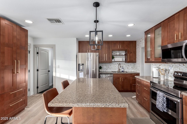 kitchen with visible vents, a kitchen bar, appliances with stainless steel finishes, light wood-style floors, and a sink