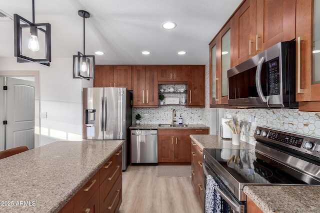 kitchen featuring pendant lighting, light wood-style flooring, a sink, appliances with stainless steel finishes, and brown cabinetry