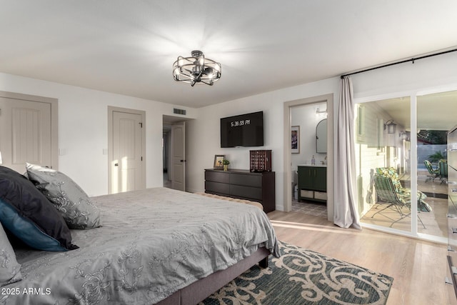 bedroom with a notable chandelier, visible vents, light wood finished floors, and connected bathroom