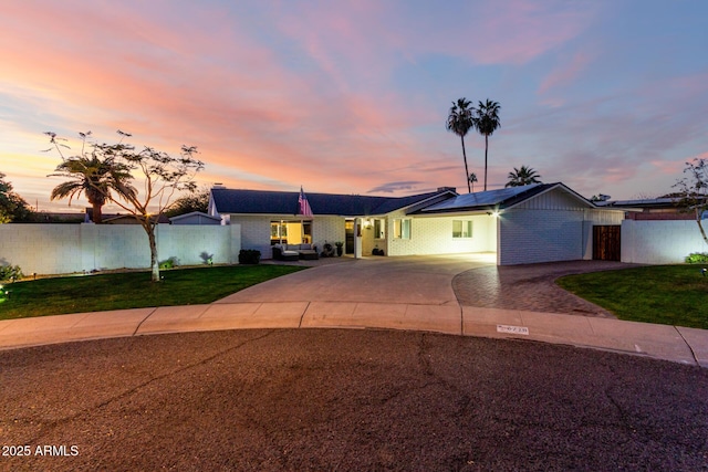 ranch-style home featuring roof mounted solar panels, concrete driveway, a front yard, and fence