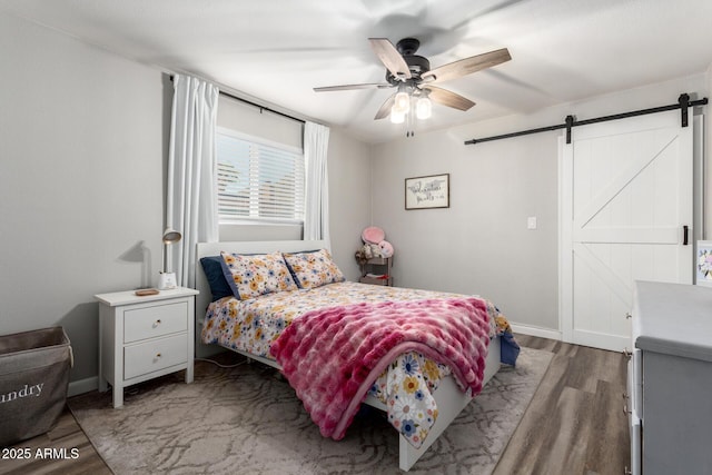 bedroom featuring a barn door, baseboards, wood finished floors, and a ceiling fan