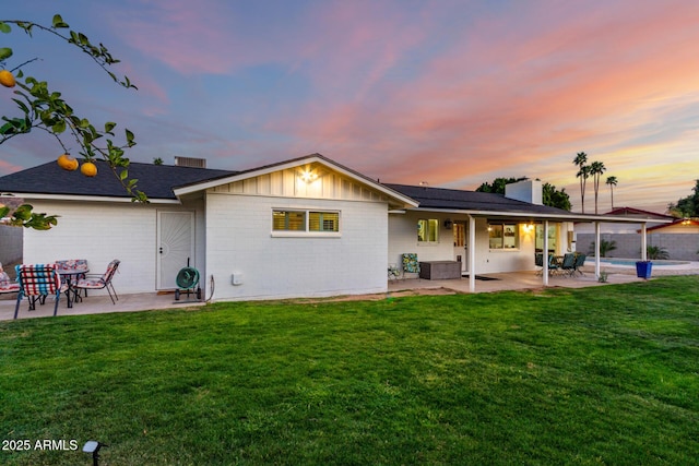 back of property at dusk with a yard, board and batten siding, and a patio area