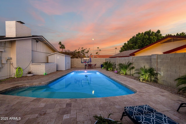 pool at dusk featuring an outdoor structure, a fenced backyard, a shed, and a patio area