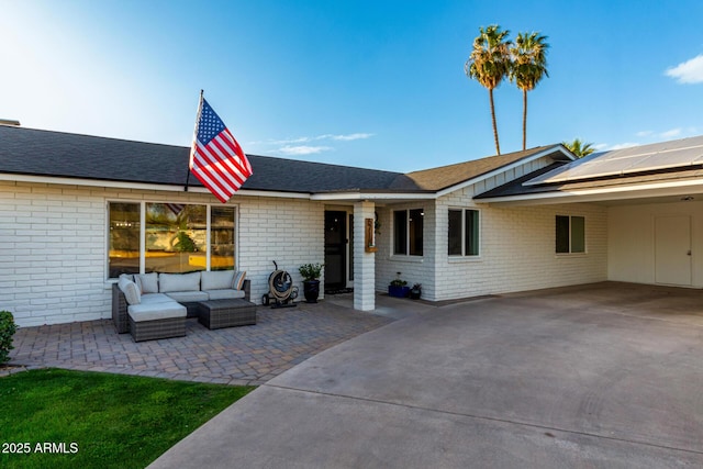 view of front facade with brick siding, solar panels, outdoor lounge area, a carport, and a patio