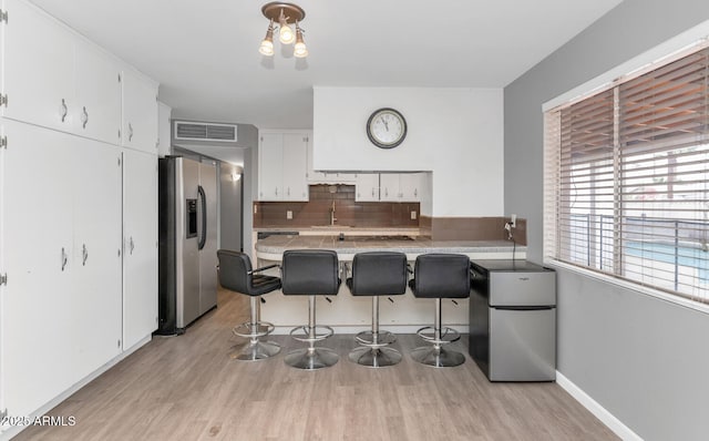 kitchen with a kitchen bar, sink, stainless steel fridge with ice dispenser, stainless steel fridge, and white cabinets