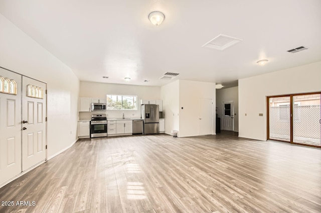 unfurnished living room with light wood-style flooring, visible vents, a sink, and attic access