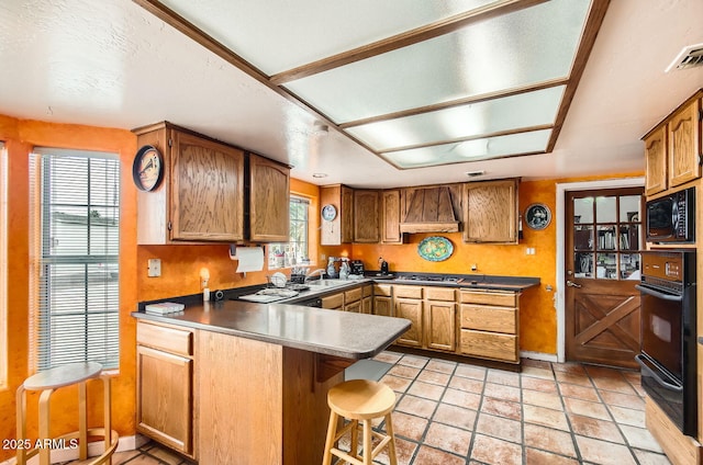 kitchen with brown cabinets, a sink, custom exhaust hood, dark countertops, and black appliances