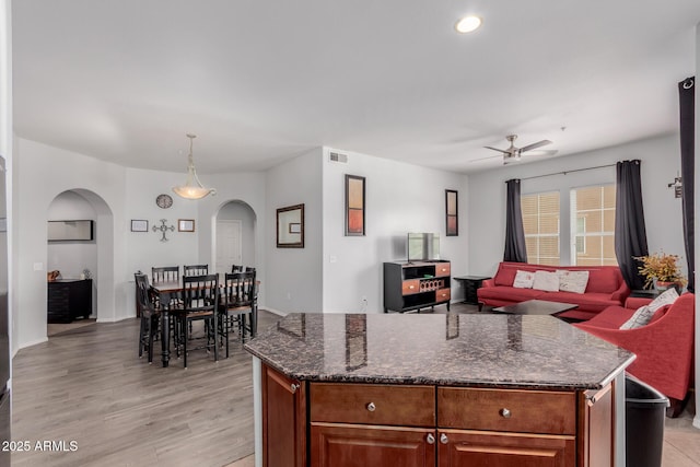 kitchen with arched walkways, a ceiling fan, open floor plan, light wood-type flooring, and visible vents