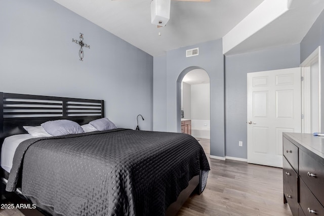 bedroom with visible vents, arched walkways, baseboards, connected bathroom, and light wood-style flooring