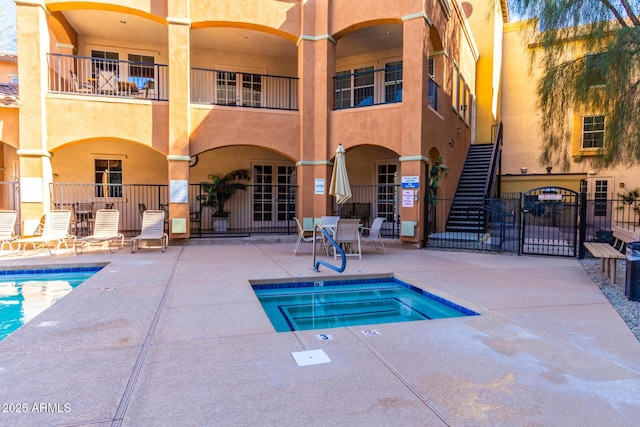 pool featuring a gate, a patio area, fence, a community hot tub, and stairs
