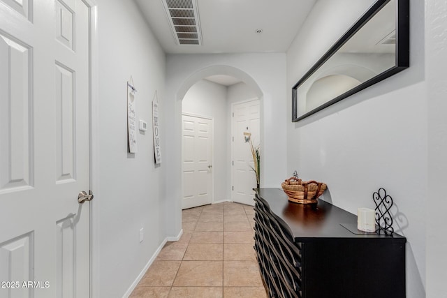 corridor featuring visible vents, arched walkways, baseboards, and light tile patterned floors