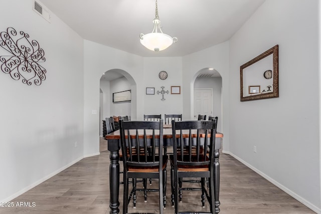 dining space featuring arched walkways, baseboards, and wood finished floors