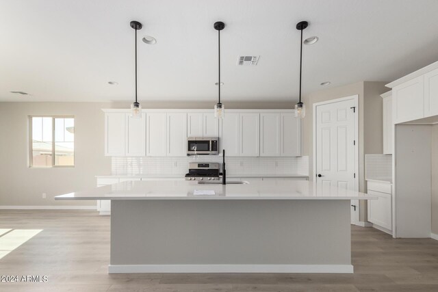 kitchen with decorative light fixtures, appliances with stainless steel finishes, light wood-type flooring, and a center island with sink