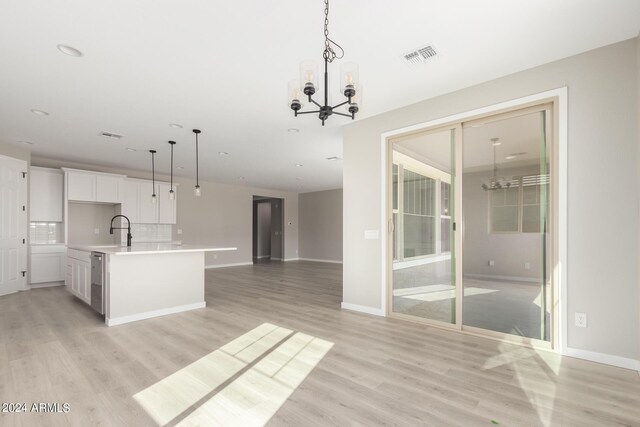 kitchen with white cabinets, pendant lighting, a center island with sink, and a notable chandelier