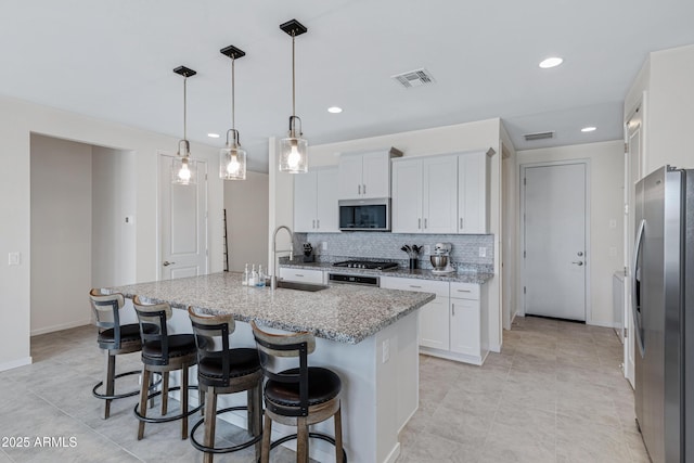 kitchen featuring visible vents, light stone counters, appliances with stainless steel finishes, a sink, and backsplash