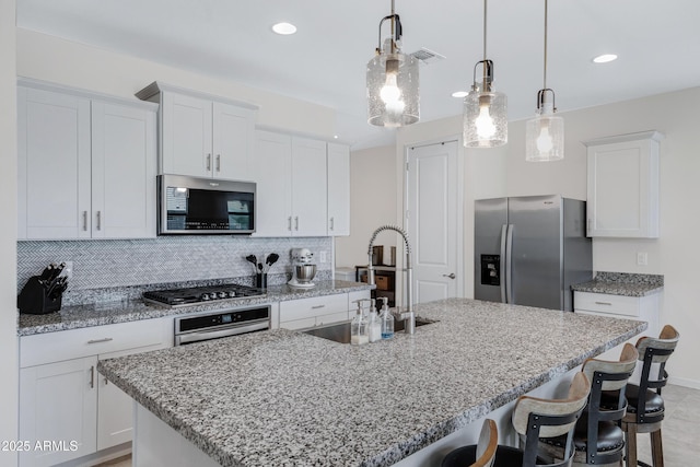 kitchen with a breakfast bar area, a sink, white cabinets, appliances with stainless steel finishes, and tasteful backsplash