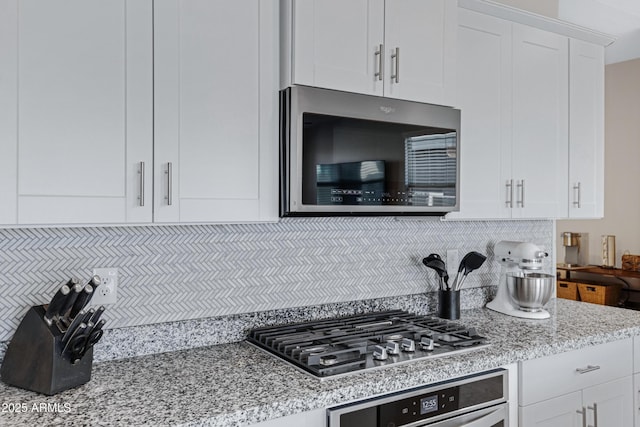 kitchen with stainless steel appliances, light stone countertops, white cabinetry, and tasteful backsplash