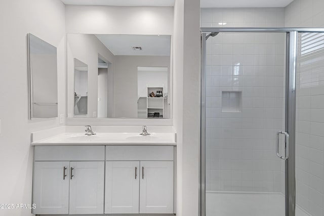 full bath featuring a stall shower, visible vents, a sink, and double vanity