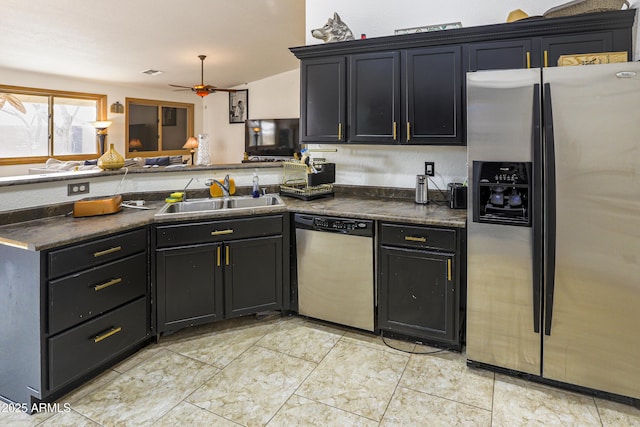 kitchen featuring dark countertops, appliances with stainless steel finishes, a sink, ceiling fan, and a peninsula