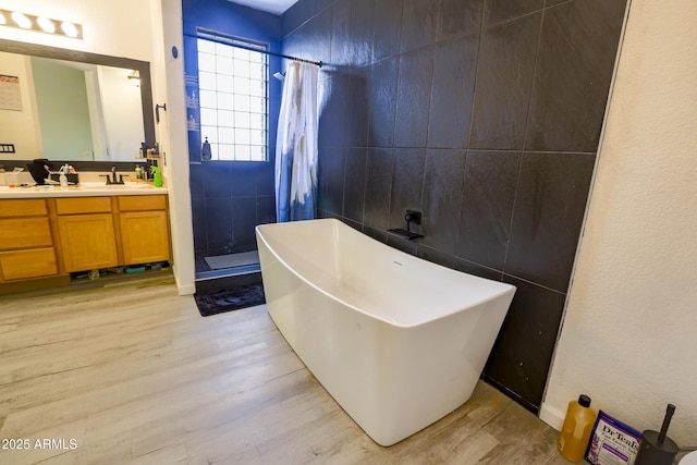 full bath with tiled shower, wood finished floors, a freestanding bath, vanity, and tile walls