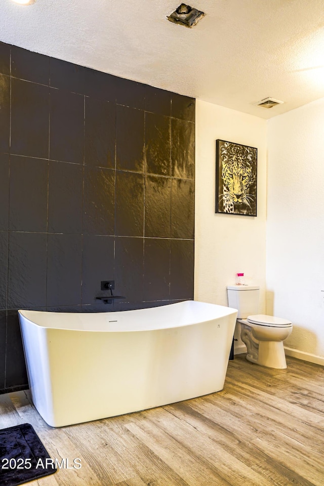 full bath with a soaking tub, a textured ceiling, toilet, and wood finished floors