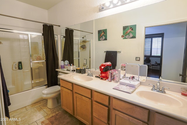 bathroom with bath / shower combo with glass door, double vanity, a sink, and toilet