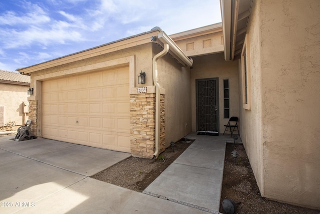 exterior space featuring a garage, stone siding, concrete driveway, and stucco siding