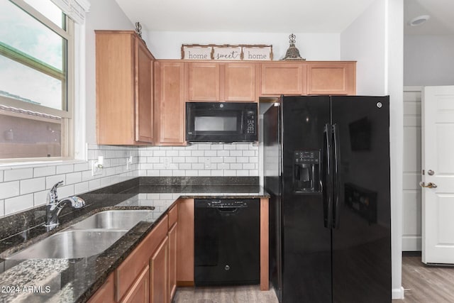 kitchen featuring sink, light hardwood / wood-style flooring, dark stone countertops, and black appliances