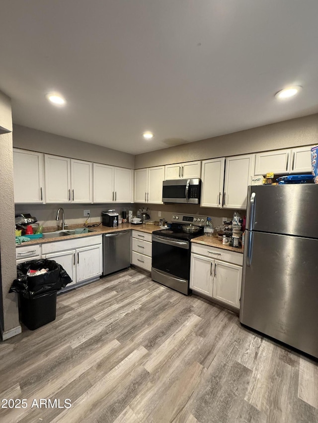 kitchen featuring white cabinetry, stainless steel appliances, sink, and light wood-type flooring