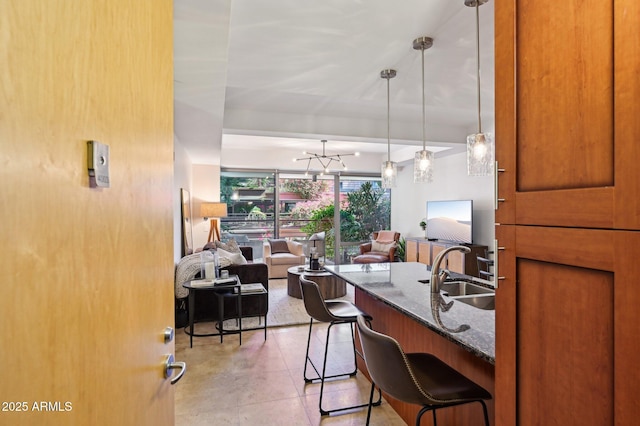 kitchen featuring a breakfast bar area, hanging light fixtures, open floor plan, a sink, and dark stone counters