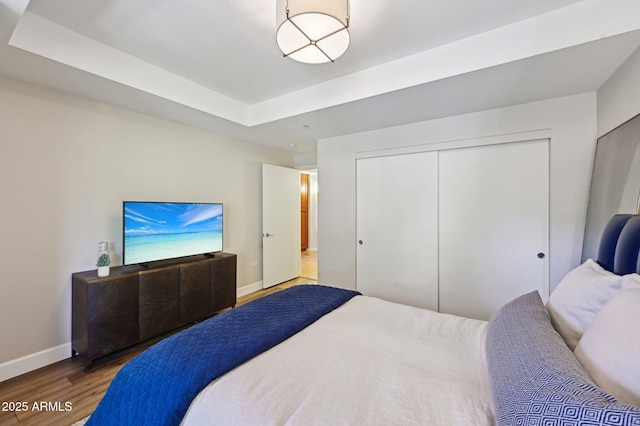 bedroom with a tray ceiling, a closet, baseboards, and wood finished floors