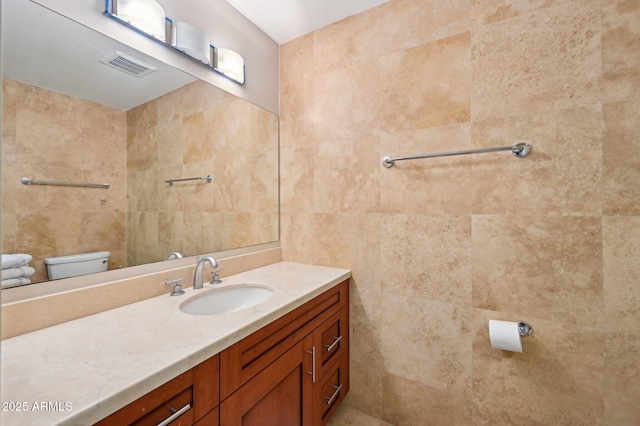 bathroom with toilet, visible vents, tile walls, and vanity