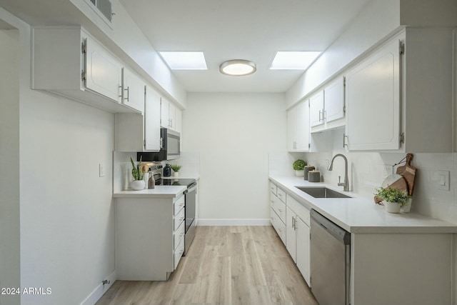 kitchen with white cabinets, sink, a skylight, light wood-type flooring, and appliances with stainless steel finishes