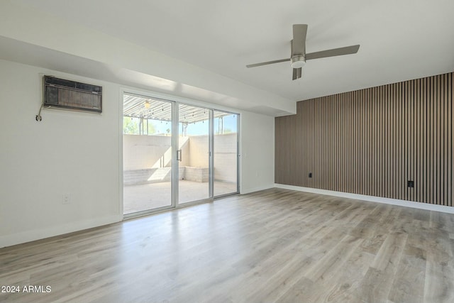 unfurnished room with a wall unit AC, wood walls, light hardwood / wood-style flooring, and ceiling fan