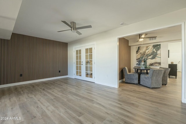 unfurnished living room featuring ceiling fan, french doors, wood walls, and light hardwood / wood-style flooring