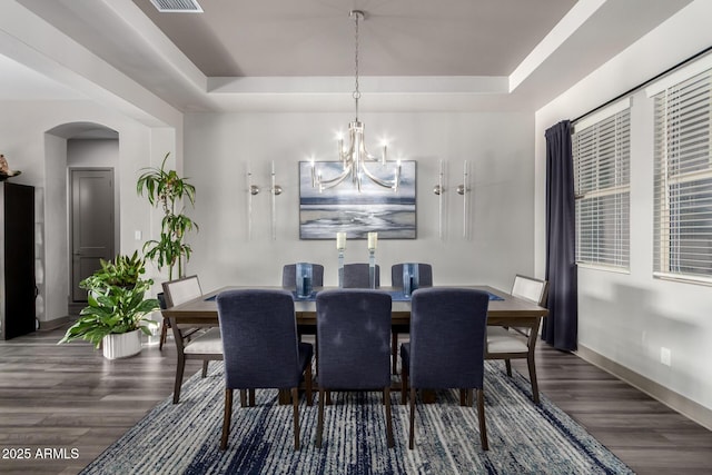 dining room featuring a tray ceiling, baseboards, arched walkways, a notable chandelier, and wood finished floors