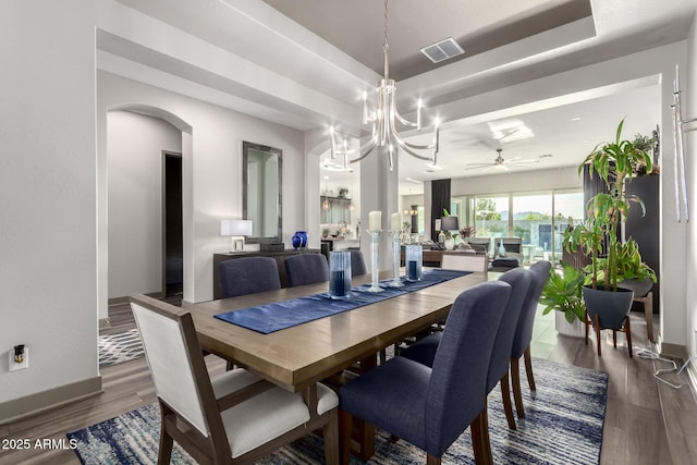 dining area featuring ceiling fan with notable chandelier, visible vents, wood finished floors, and a raised ceiling
