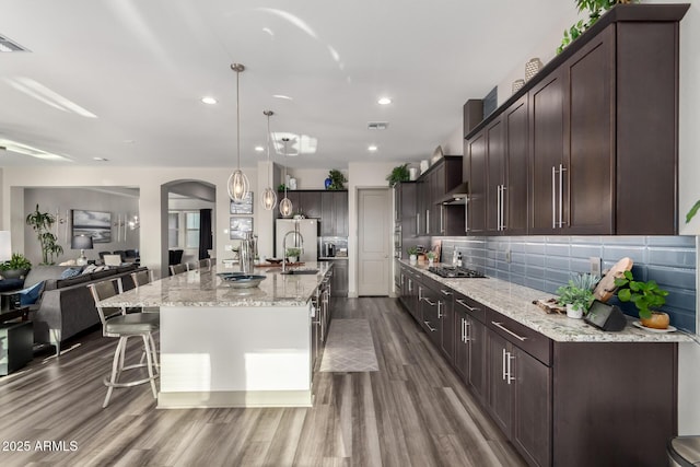 kitchen with dark wood finished floors, backsplash, light stone countertops, dark brown cabinetry, and wall chimney exhaust hood