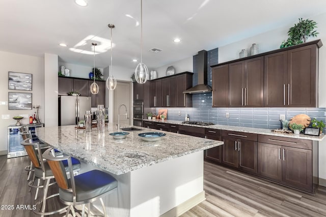 kitchen featuring a spacious island, backsplash, a sink, wall chimney range hood, and appliances with stainless steel finishes